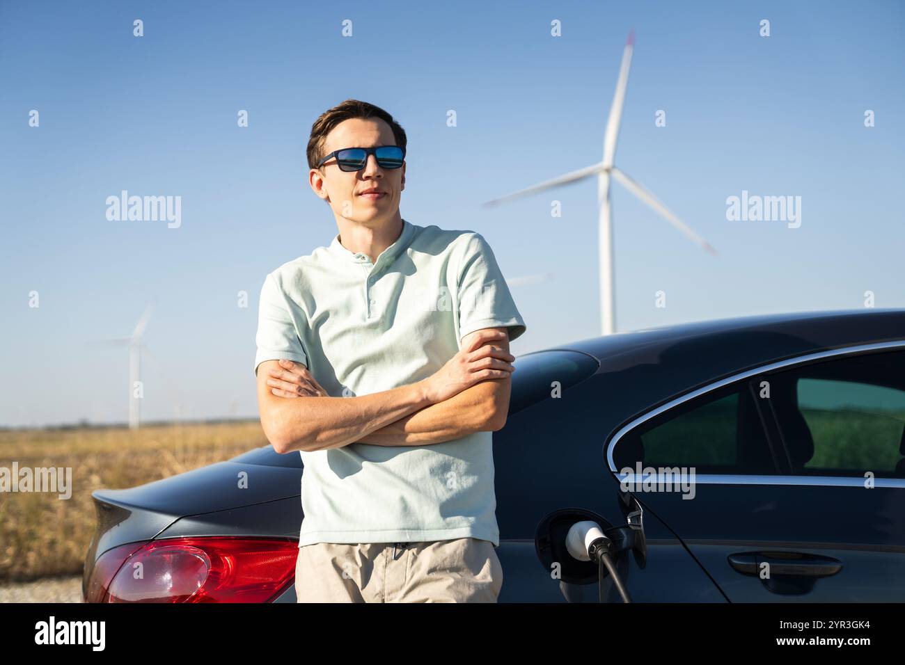 Homme avec voiture électrique de charge. Éoliennes en arrière-plan. Banque D'Images