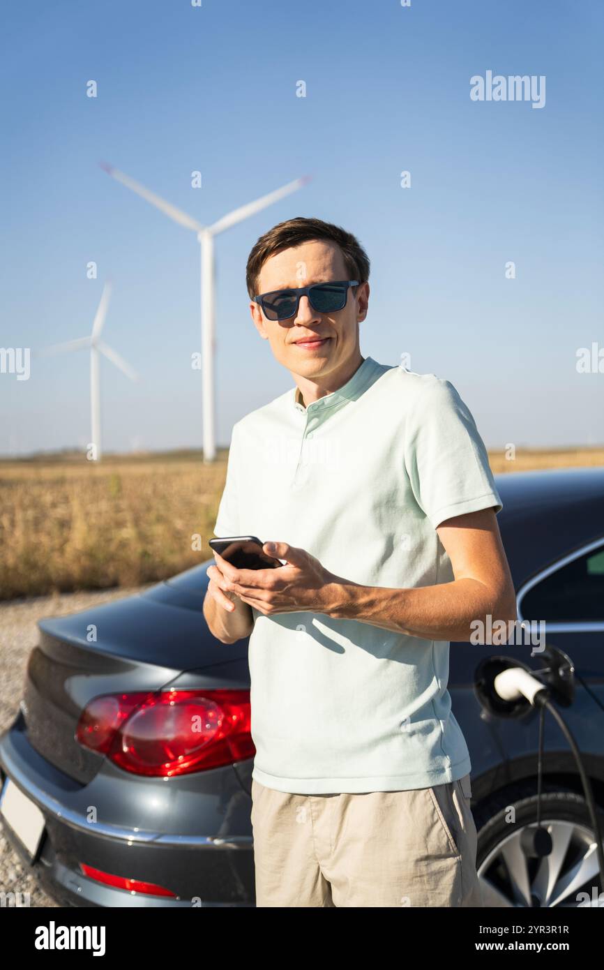 Homme avec voiture électrique de charge. Éoliennes en arrière-plan. Banque D'Images