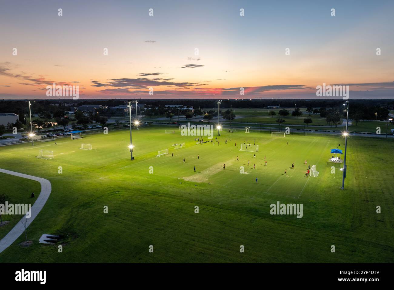 Sportifs jouant un match de football sur le stade illuminé dans le parc sportif public Banque D'Images