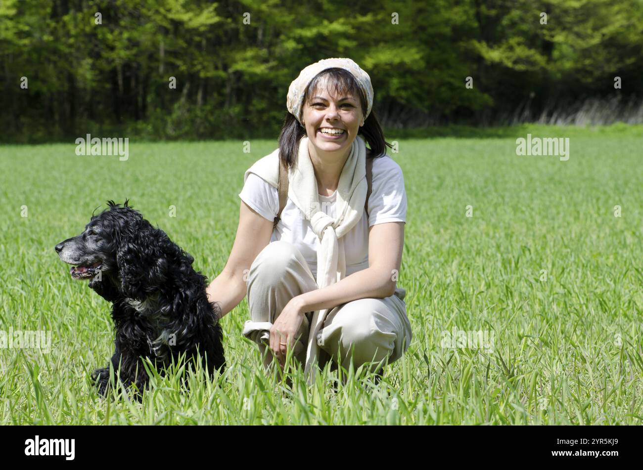 Femme heureuse avec un foulard et sac à dos et son chien sur le champ vert dans une journée d'été ensoleillée à Locarno, Tessin, Suisse, Europe Banque D'Images