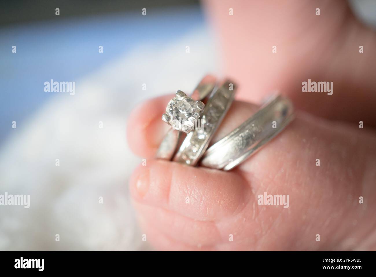 Les minuscules orteils du nouveau-né tiennent les anneaux de mariage des parents Banque D'Images