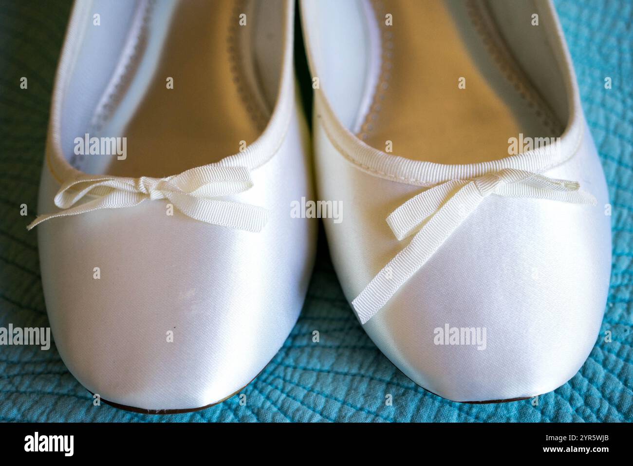 Gros plan de ballerines blanches en satin avec des noeuds de ruban sur fond bleu Banque D'Images