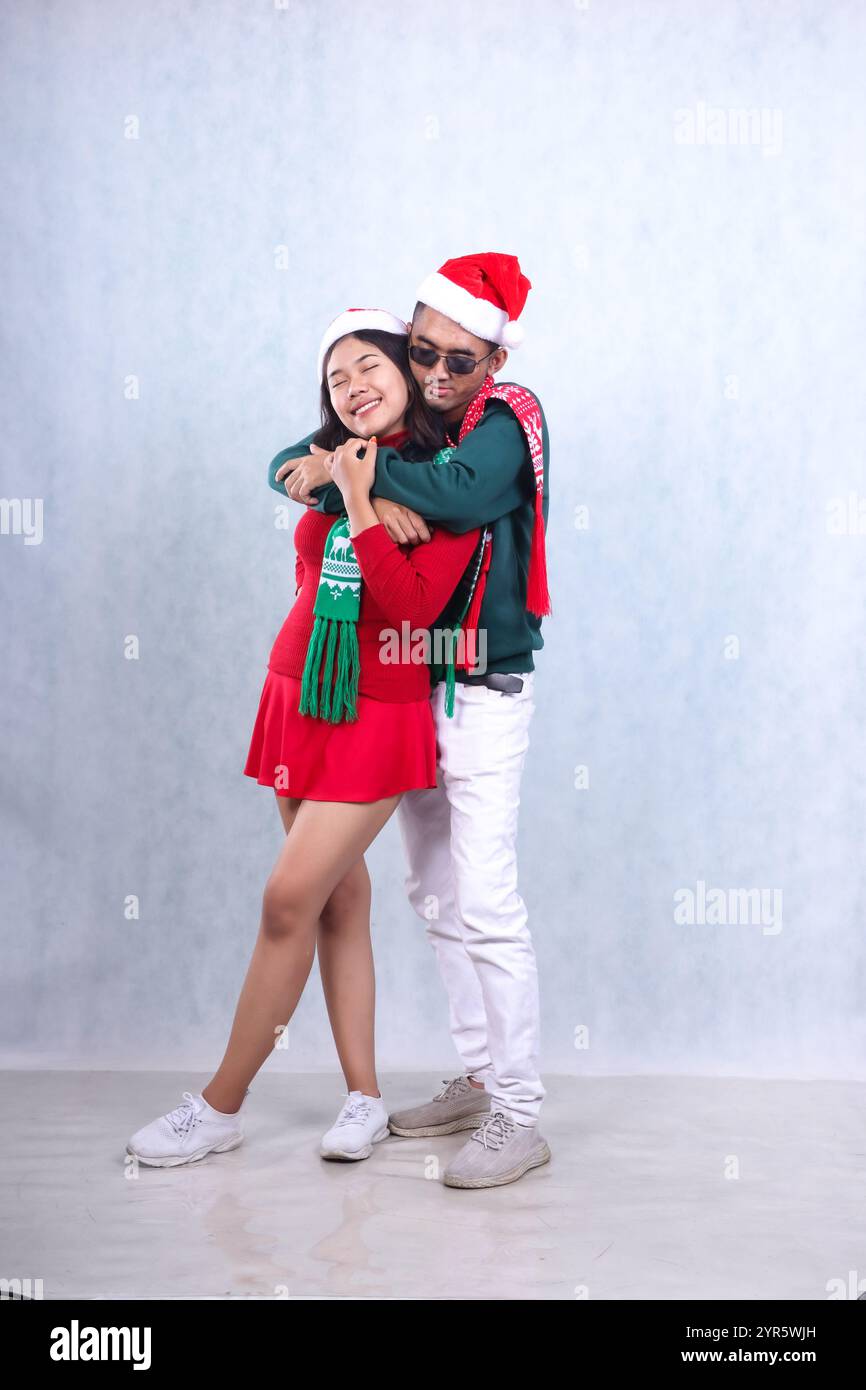 Corps entier deux personnes asiatiques portant des chapeaux de Père Noël et des vêtements chauds, debout avec les yeux fermés serrés par derrière tout en fermant les yeux, célébrant Christma Banque D'Images