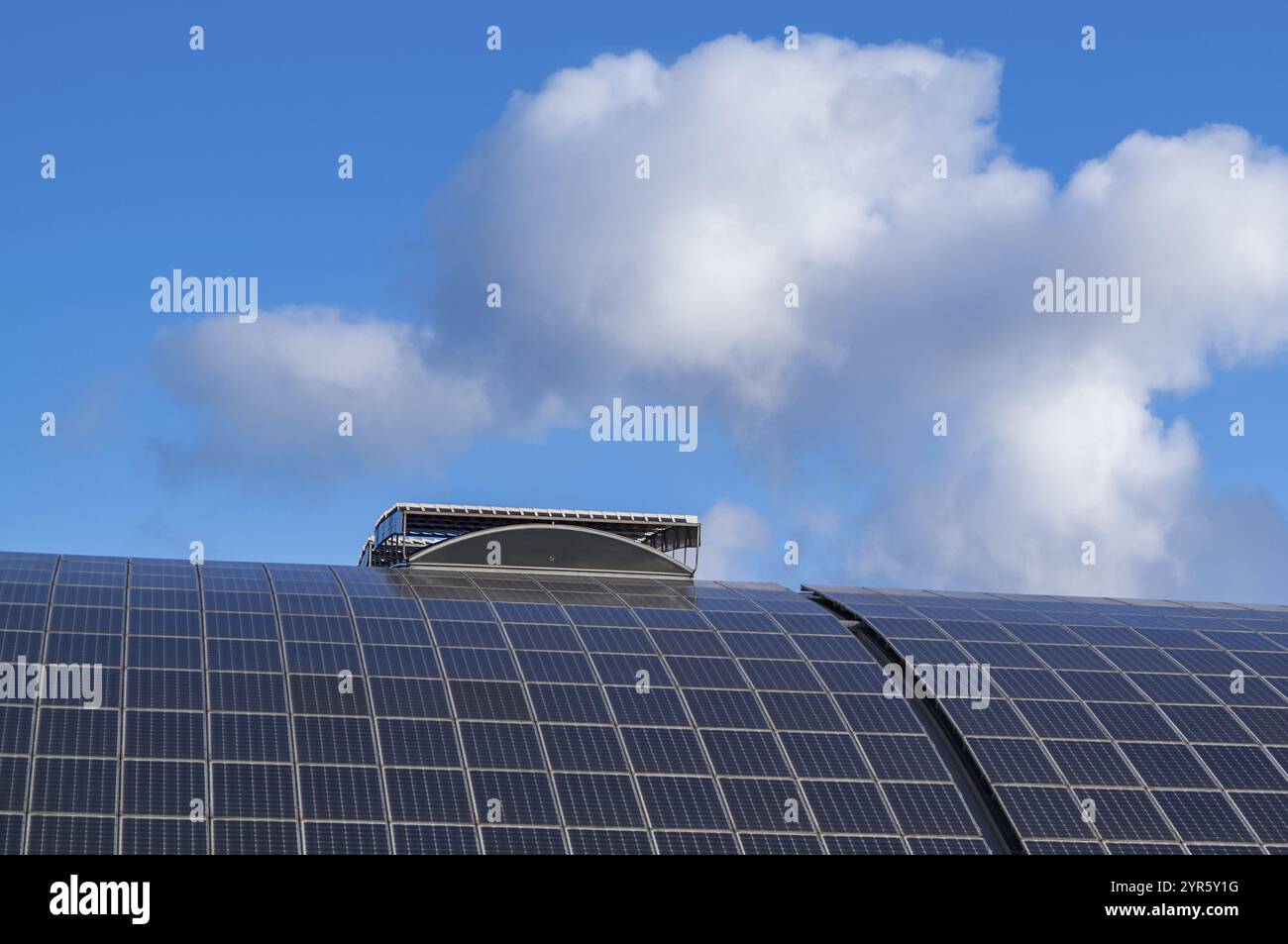 Les panneaux solaires incurvés installés sur un toit génèrent de l’énergie propre sous un ciel bleu nuageux, mettant en valeur des pratiques énergétiques durables Banque D'Images