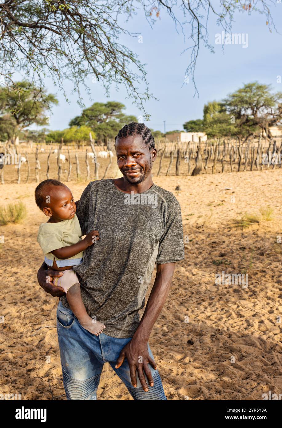 homme africain du village tenant un bébé à la ferme devant l'enclos à bétail Banque D'Images