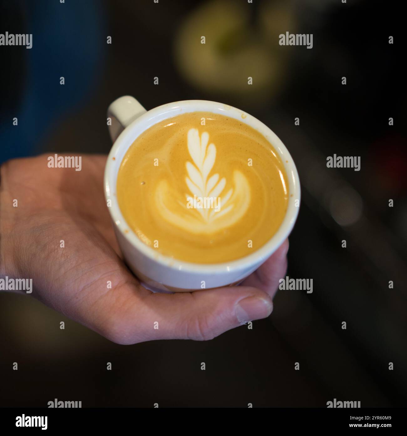 Barista tenant un Latte fraîchement préparé avec Leaf Latte Art Banque D'Images