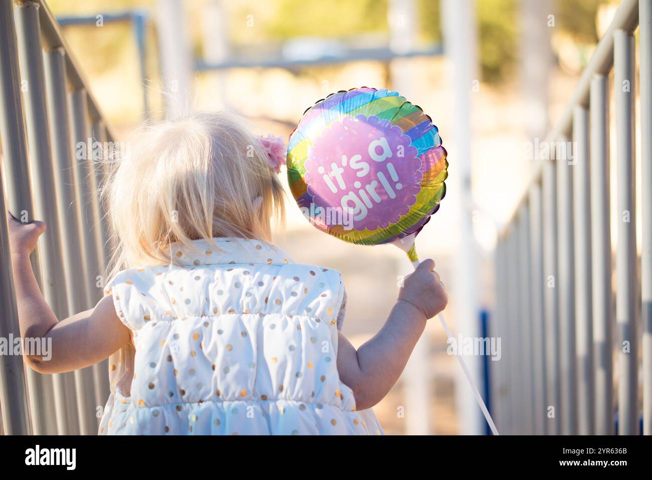 Annonce de bébé avec 'C'est une fille!' Ballon tenu par le tout-petit en extérieur Banque D'Images