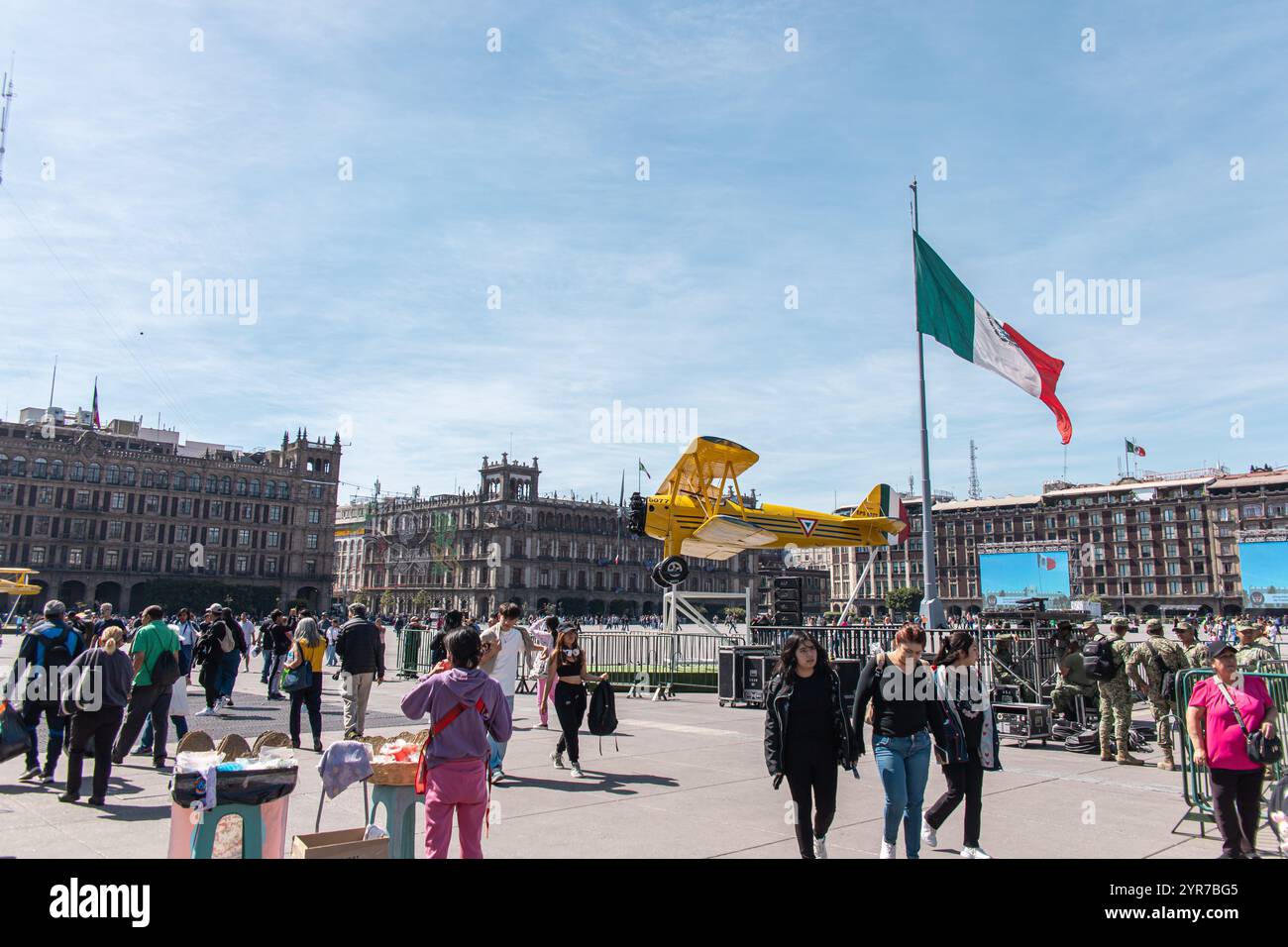 Une scène animée à Zócalo Plaza avec un affichage d'avion jaune pour les célébrations du jour de la Révolution, le drapeau mexicain et les bâtiments historiques. Banque D'Images