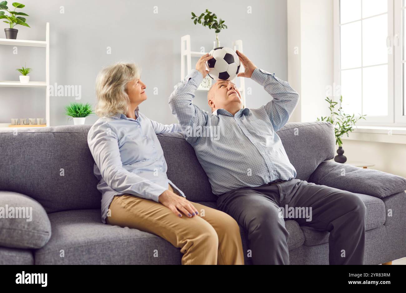 Couple senior retraité assis sur le canapé dans le salon à la maison et s'amuser avec le ballon de football. Banque D'Images