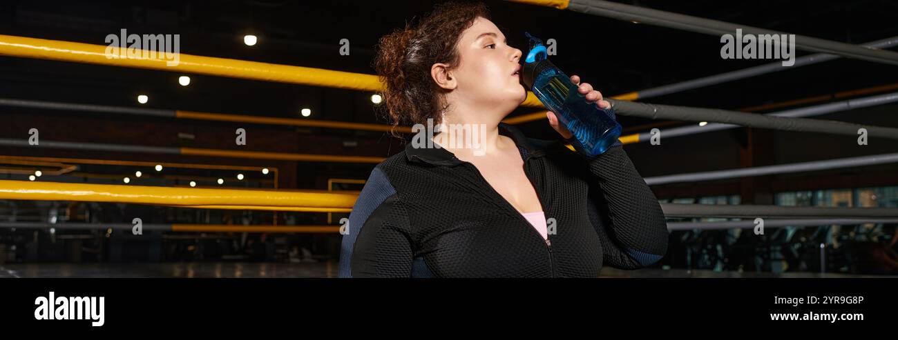 Une femme dévouée fait une pause pour s'hydrater tout en étant engagée dans une routine d'entraînement vigoureuse au gymnase. Banque D'Images