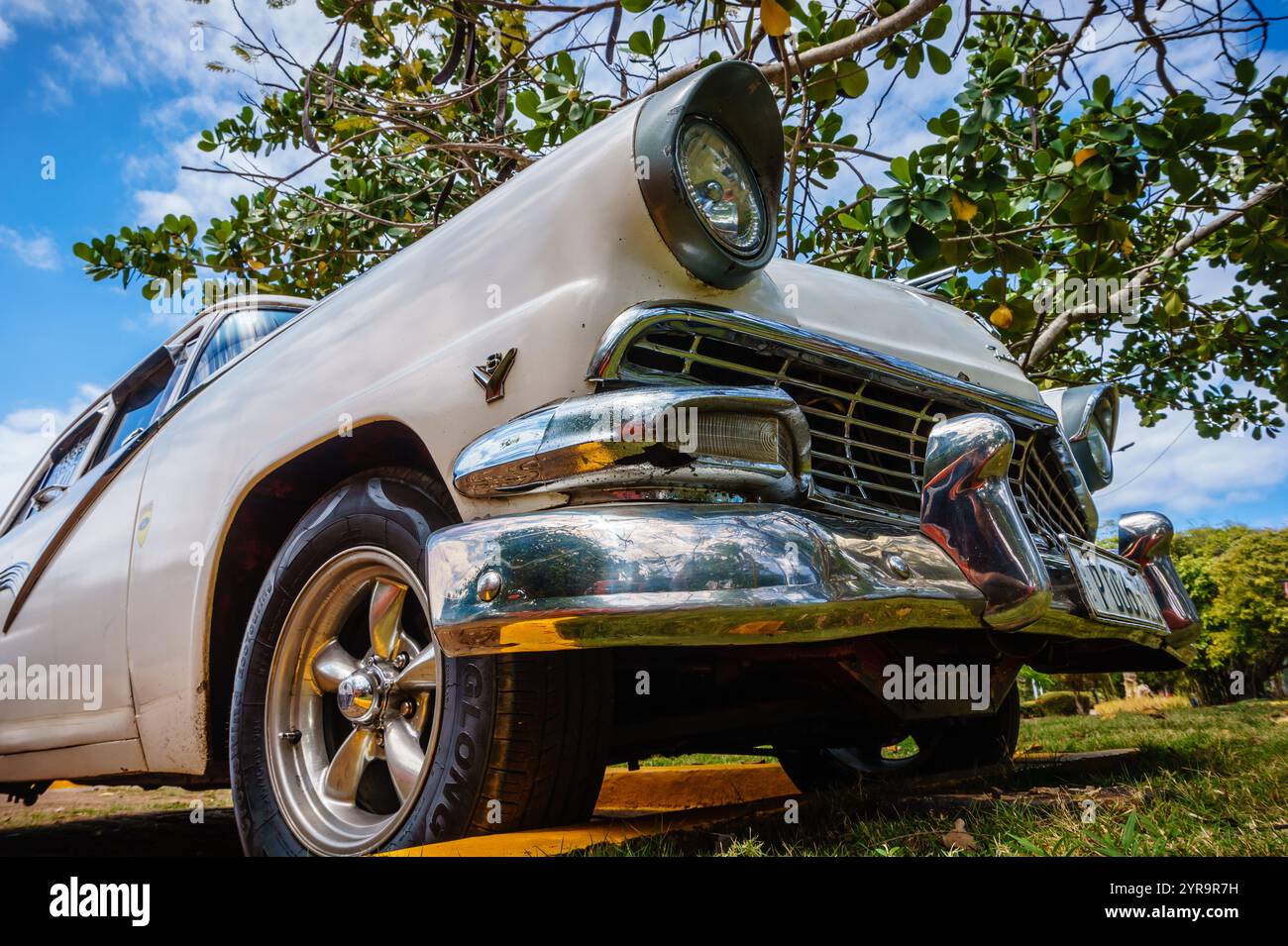 Une voiture ancienne est garée dans une zone herbeuse. La voiture est blanche et a une finition chromée. Le coffre est ouvert et le capot relevé. La voiture est garée sous un t Banque D'Images