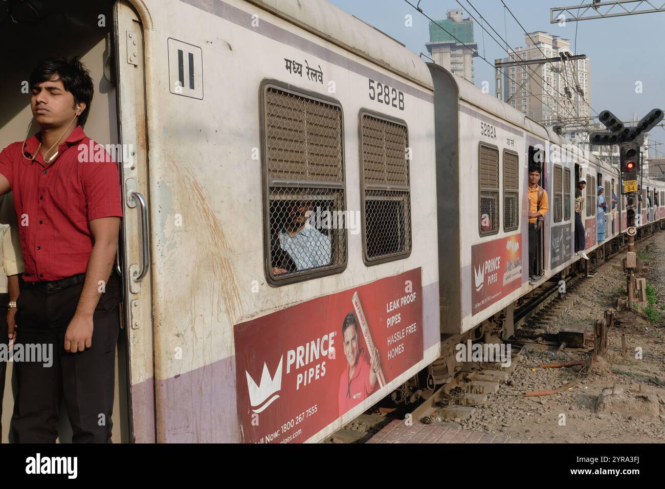 Mumbai, Inde : un passager masculin écoutant avec des écouteurs se tient à la porte ouverte d'un train de banlieue roulant dans Chhatrapati Shivaji Maharaj Terminus Banque D'Images