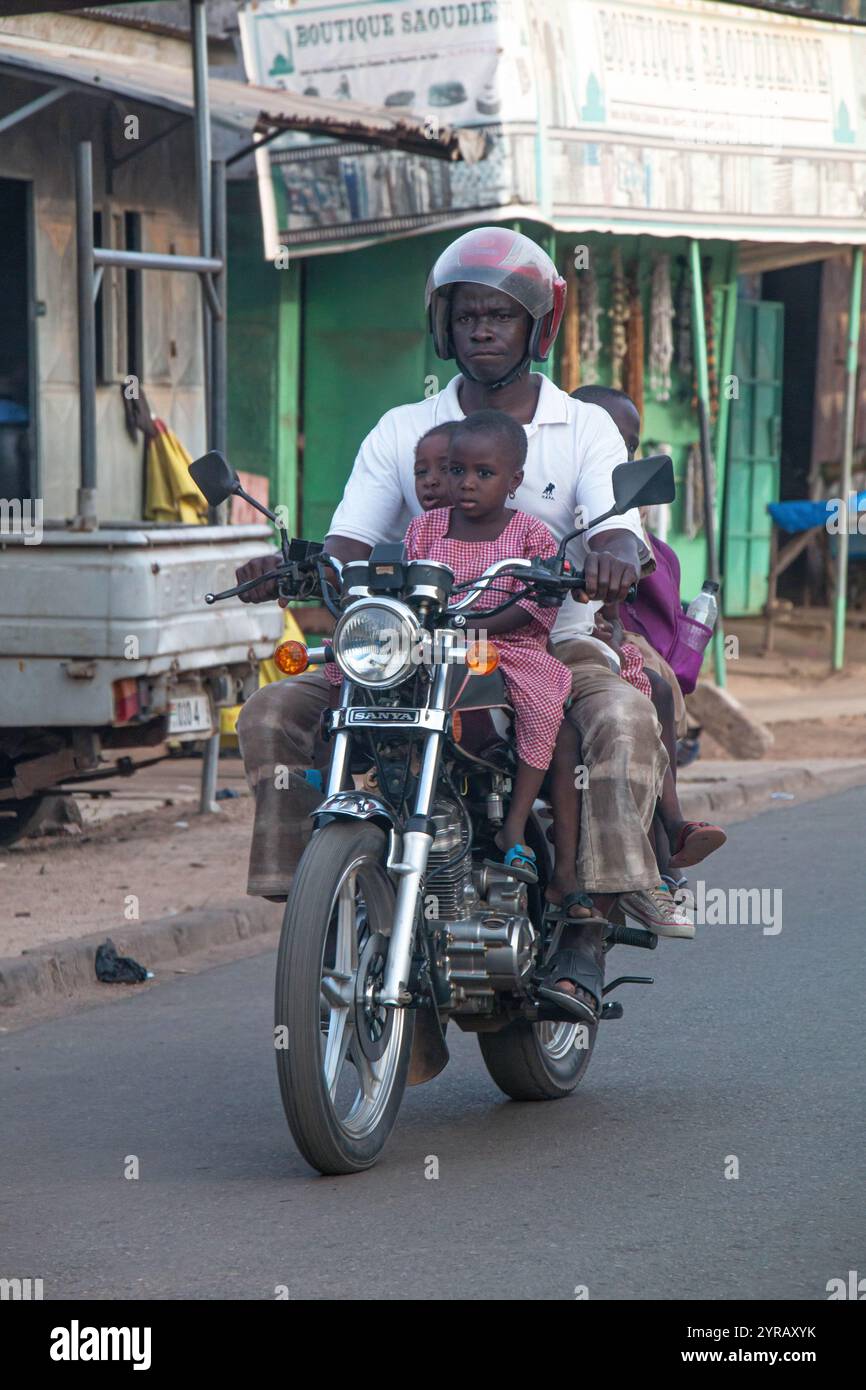 Père et enfants conduisant une moto dans une rue africaine urbaine au Togo, capturant la vie quotidienne, le regroupement familial et la culture des transports locaux Banque D'Images