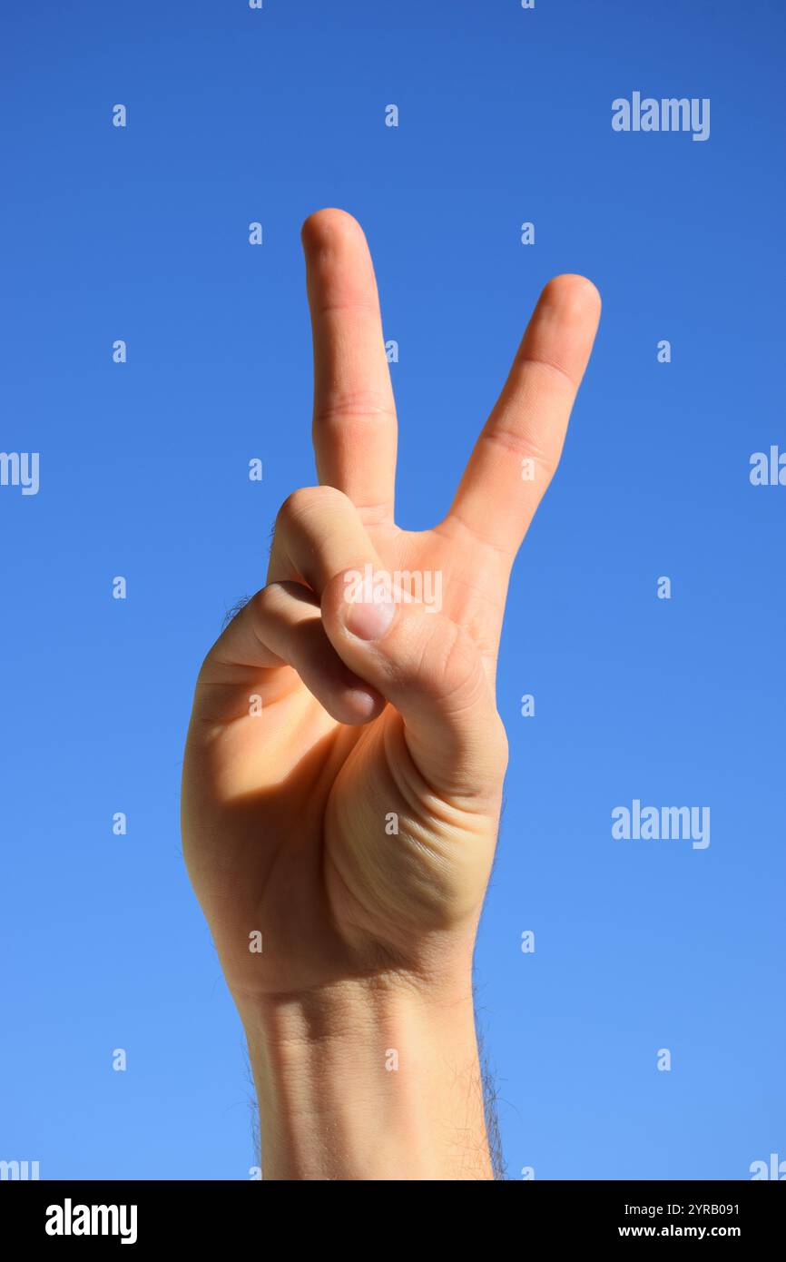 Une main faisant le signe de la paix contre un ciel bleu vif. Banque D'Images