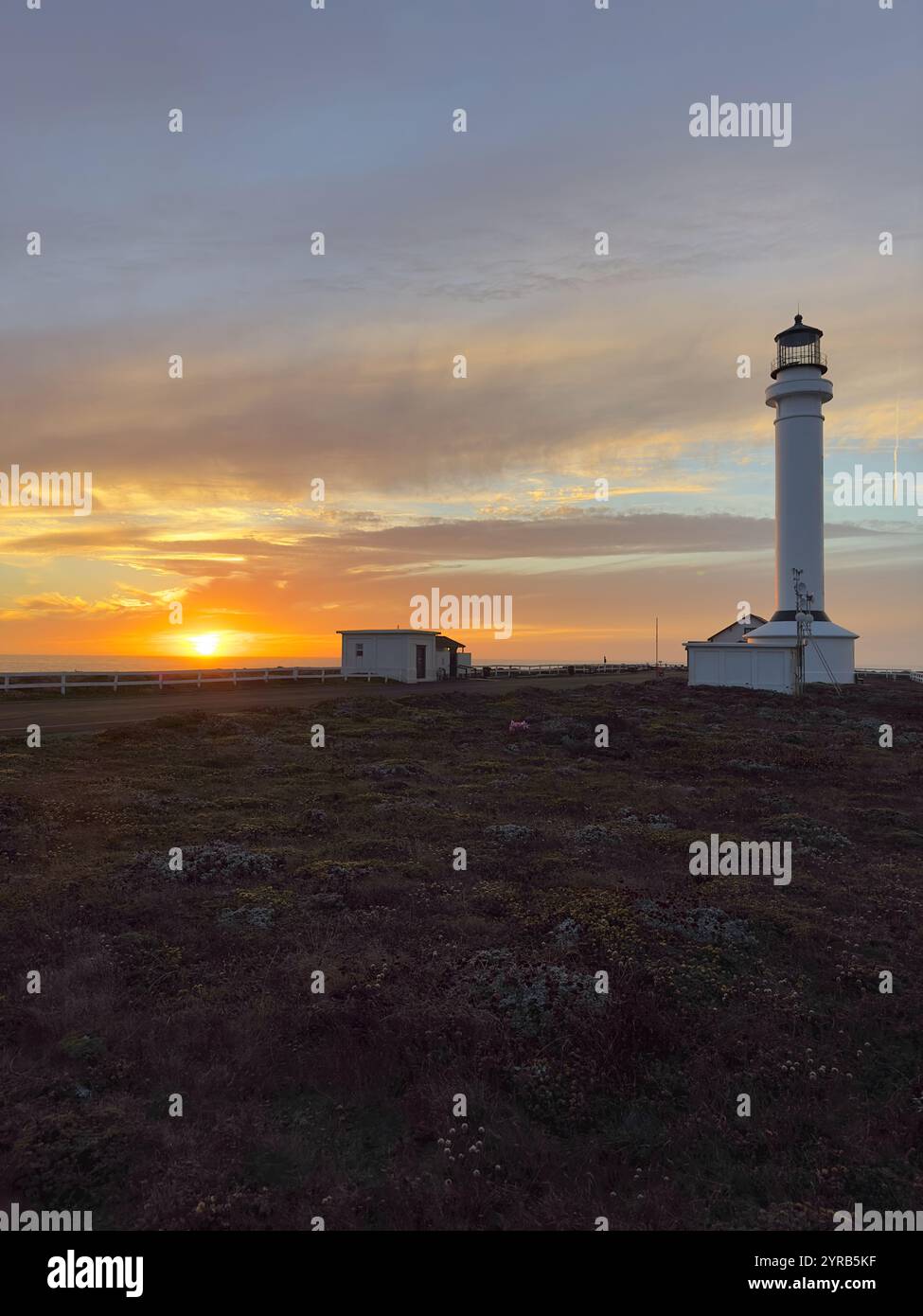 Le phare de point Arena projette une silhouette sur un ciel de coucher de soleil vibrant. La lumière dorée crée une scène à couper le souffle sur la côte accidentée de Mendocino. - Image de stock capturée avec un smartphone