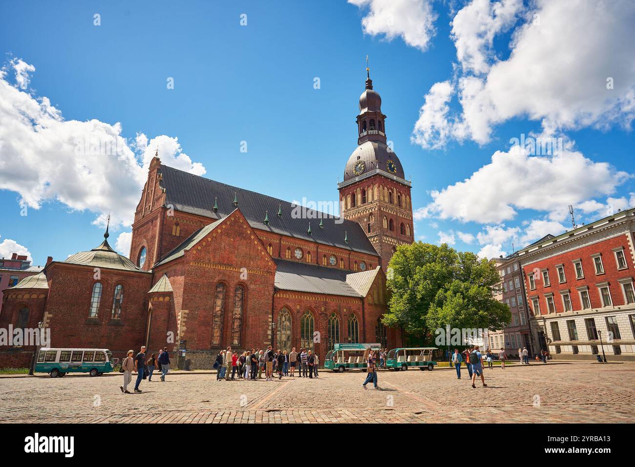 Une scène vibrante à Riga, Lettonie, avec une église historique en briques avec une grande tour de l'horloge, entourée d'une place pavée remplie de visiteurs et Banque D'Images