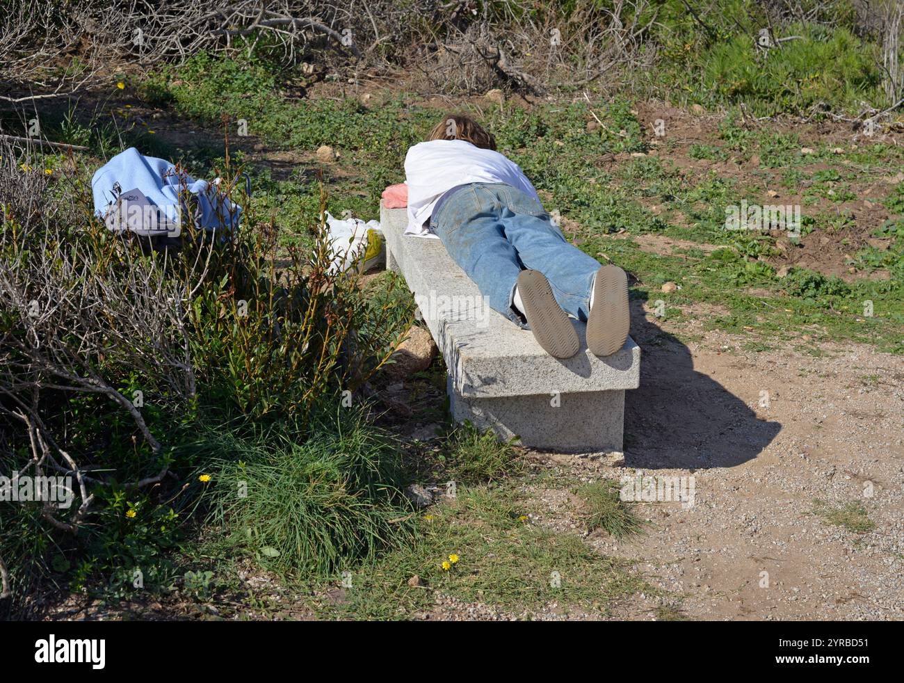 jeune homme repose allongé sur un banc de pierre dans un parc Banque D'Images