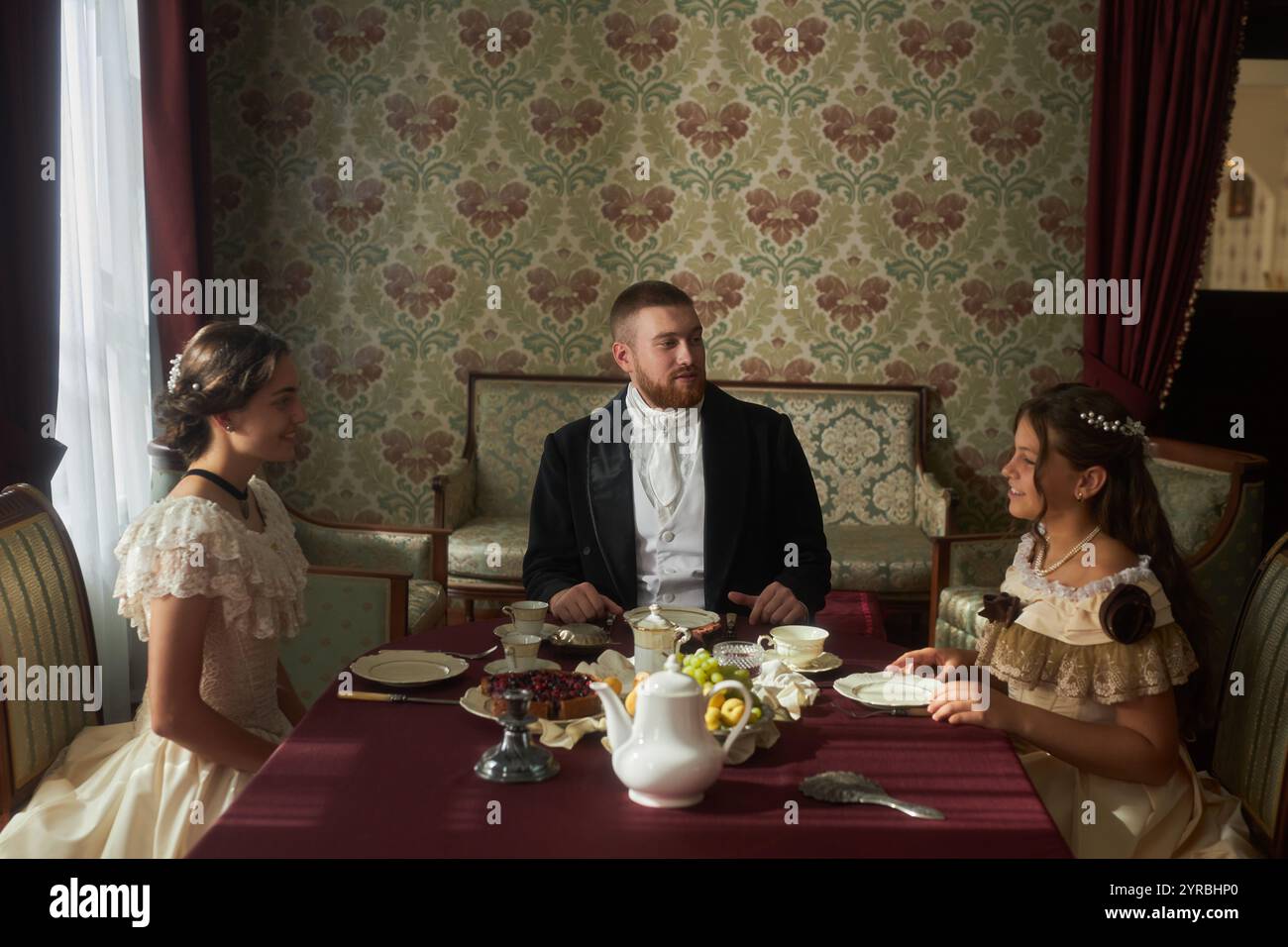 Scène de groupe à table avec trois personnages élégamment habillés conversant dans un intérieur classique Banque D'Images