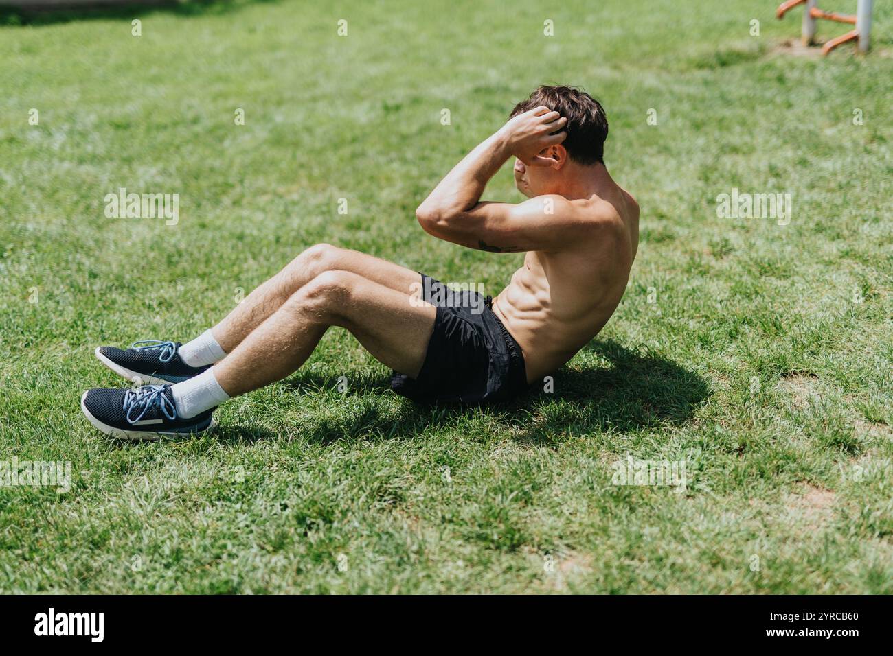 Homme en forme s'exerçant à l'extérieur effectuant des sit-ups sur un terrain herbeux Banque D'Images
