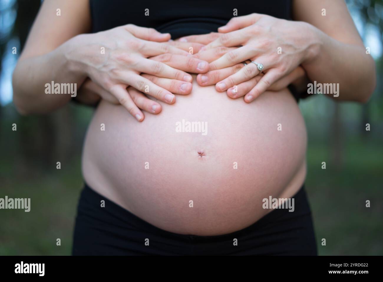 Femme enceinte avec les mains sur le ventre à l'extérieur - maternité et liaison familiale Banque D'Images