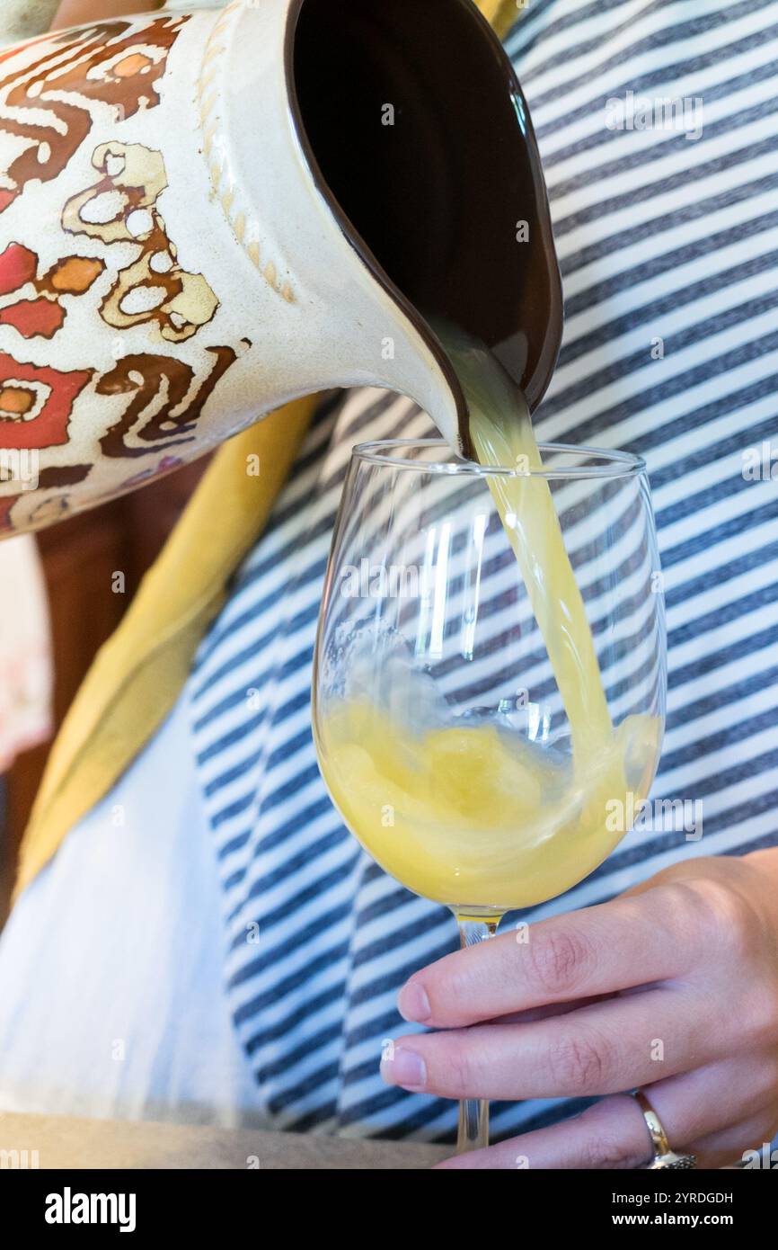 Verser du jus d'orange frais d'un pichet décoratif dans un verre à vin Banque D'Images