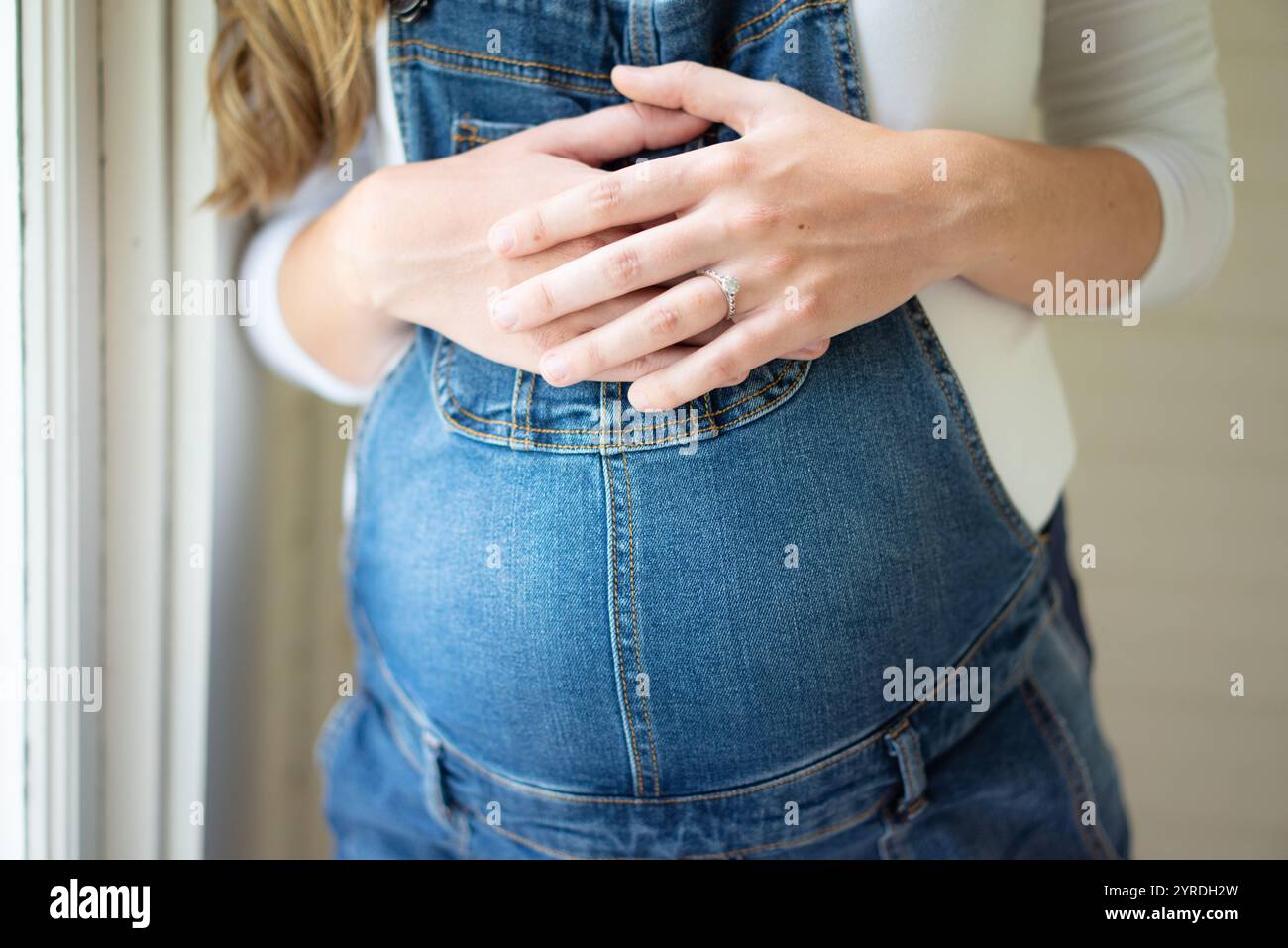 Gros plan des mains d'une femme enceinte sur le ventre dans des combinaisons denim Banque D'Images