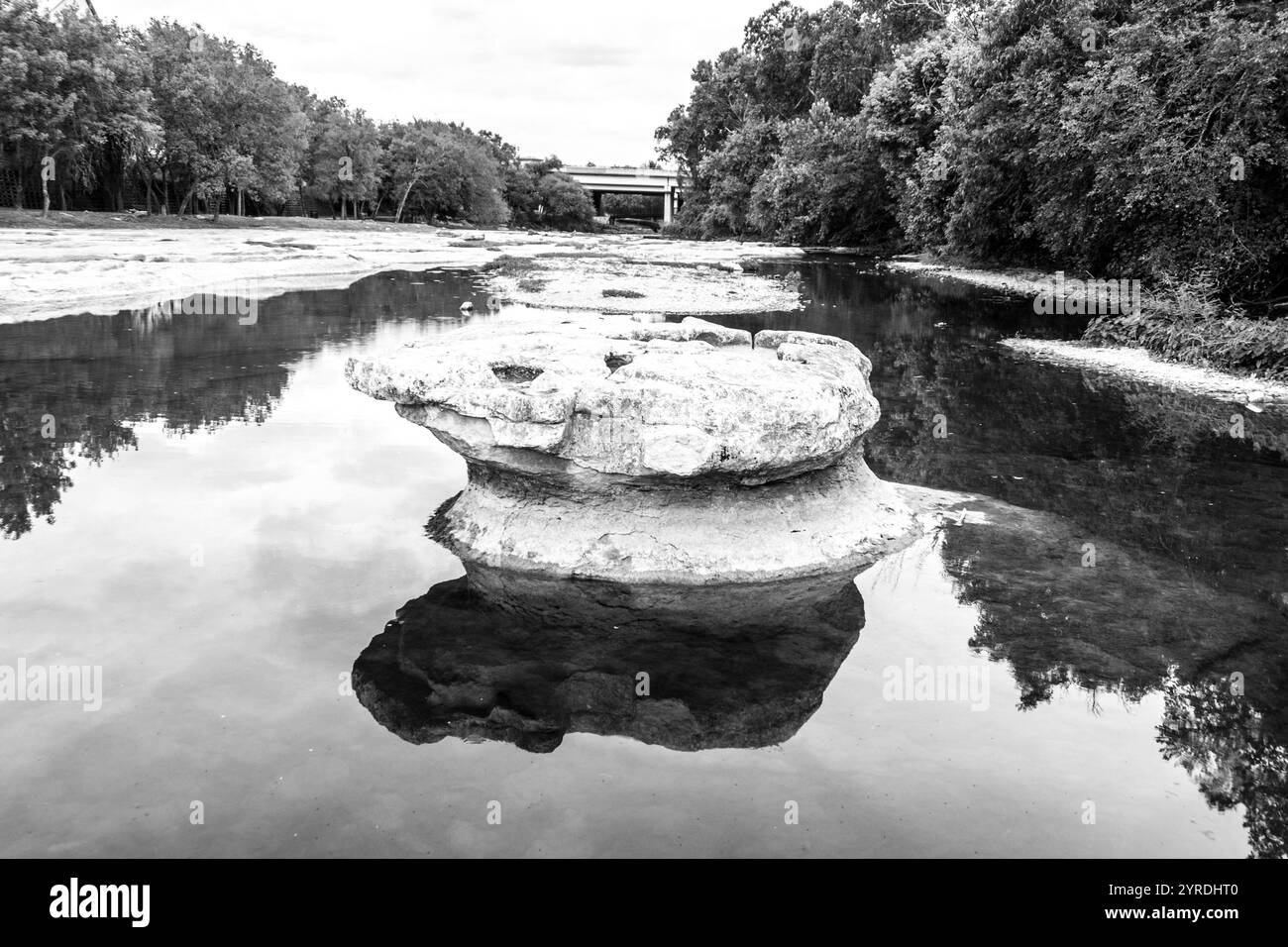 Formation de roche solitaire reflétant dans Tranquil River - photographie de la nature en noir et blanc Banque D'Images