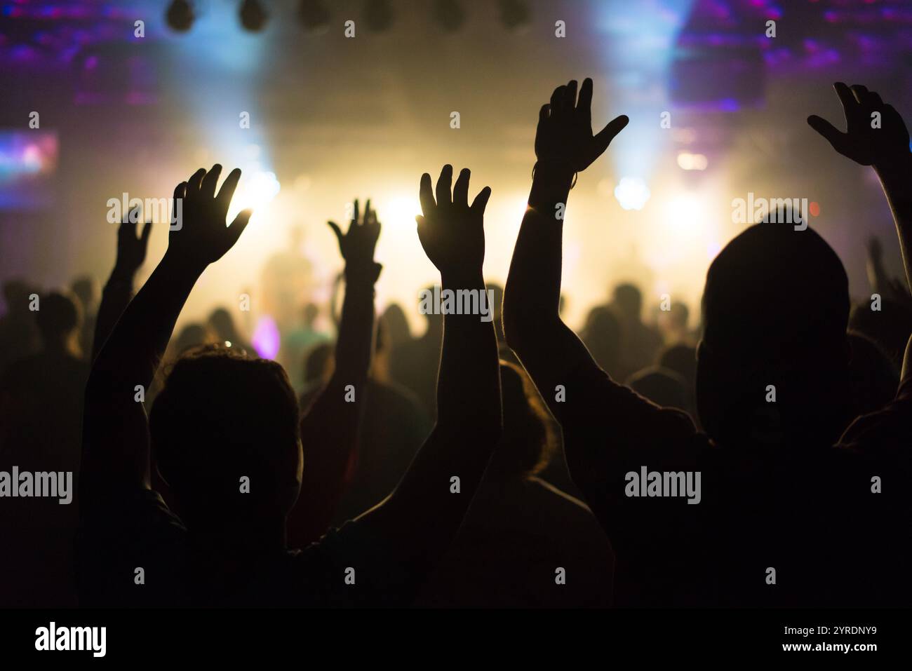 Silhouettes de personnes vénérant avec les mains levées dans un concert ou un service de culte Banque D'Images