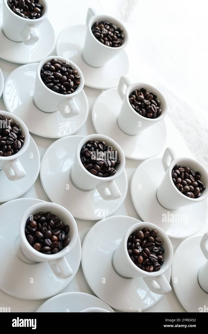 Tasses à café blanches avec des grains de café disposés sur une table blanche Banque D'Images