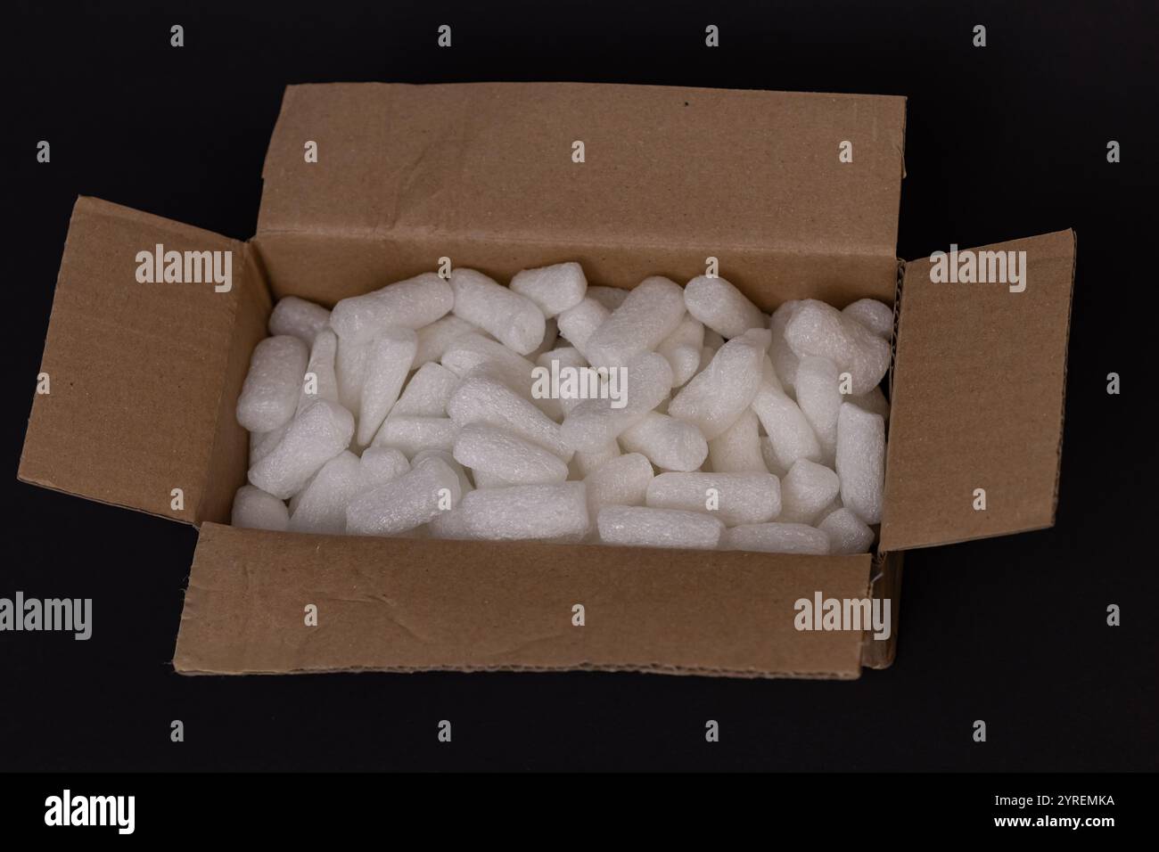 Boîte en carton remplie d'arachides d'emballage en mousse blanche pour un emballage et un transport sécurisés sur un fond sombre Banque D'Images