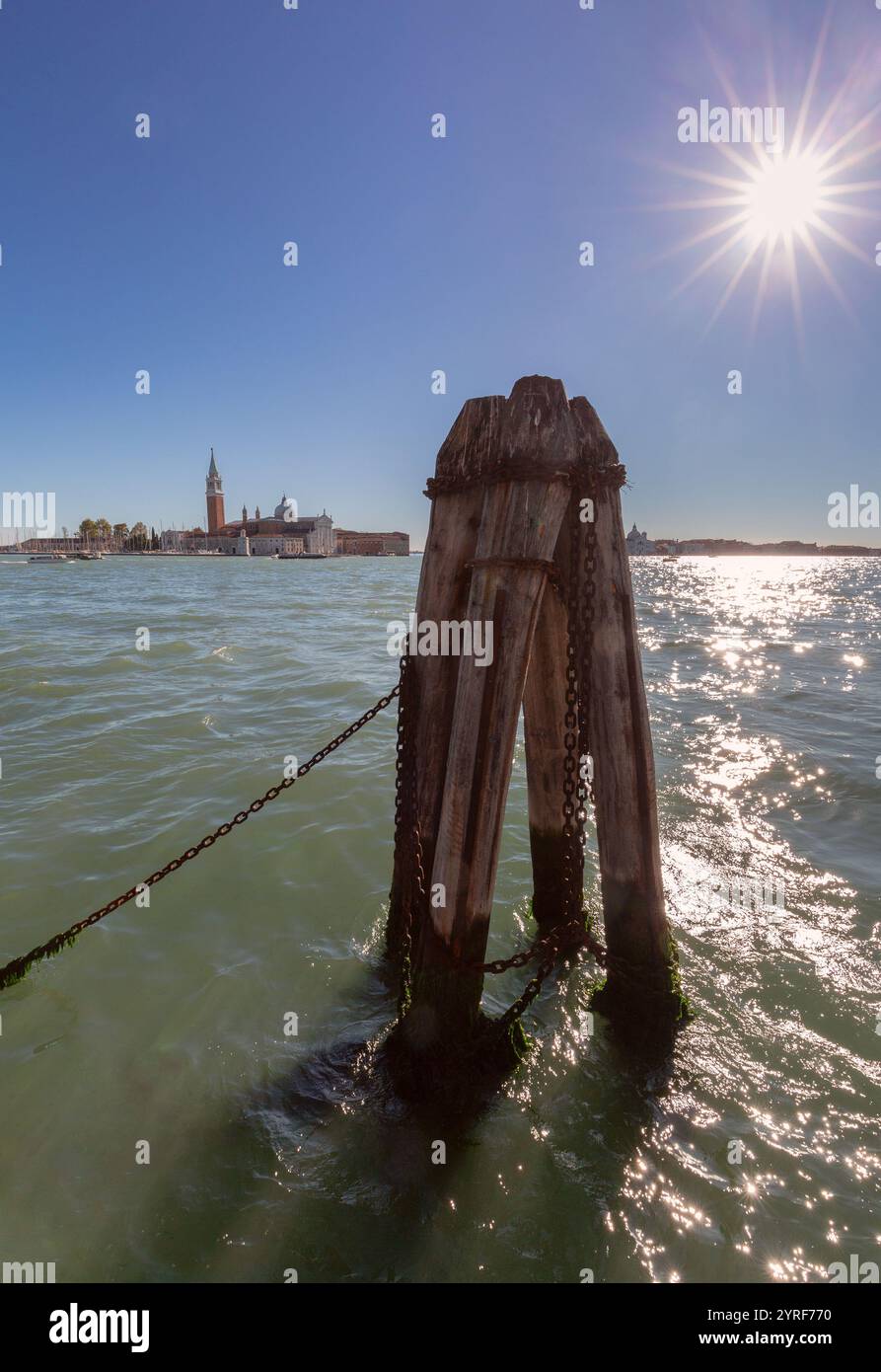 Jetée en bois avec des chaînes au premier plan et Basilique de San Giorgio Maggiore vue à travers la lagune vénitienne à Venise, sous un soleil éclatant et un ciel bleu clair, Italie Banque D'Images
