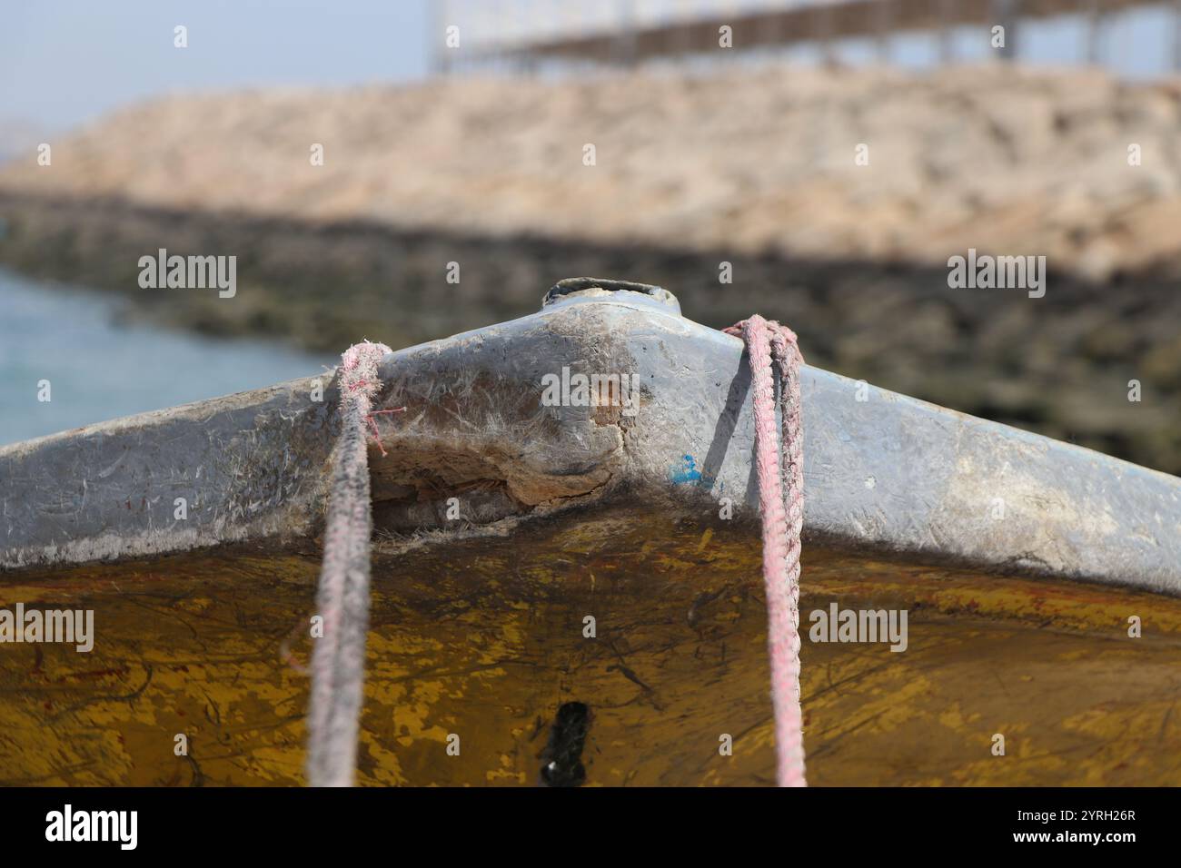 Un bateau altéré avec des cordes rustiques amarré sur la rive de l'île de Qeshm, mettant en valeur la beauté sauvage de la vie maritime traditionnelle. Banque D'Images