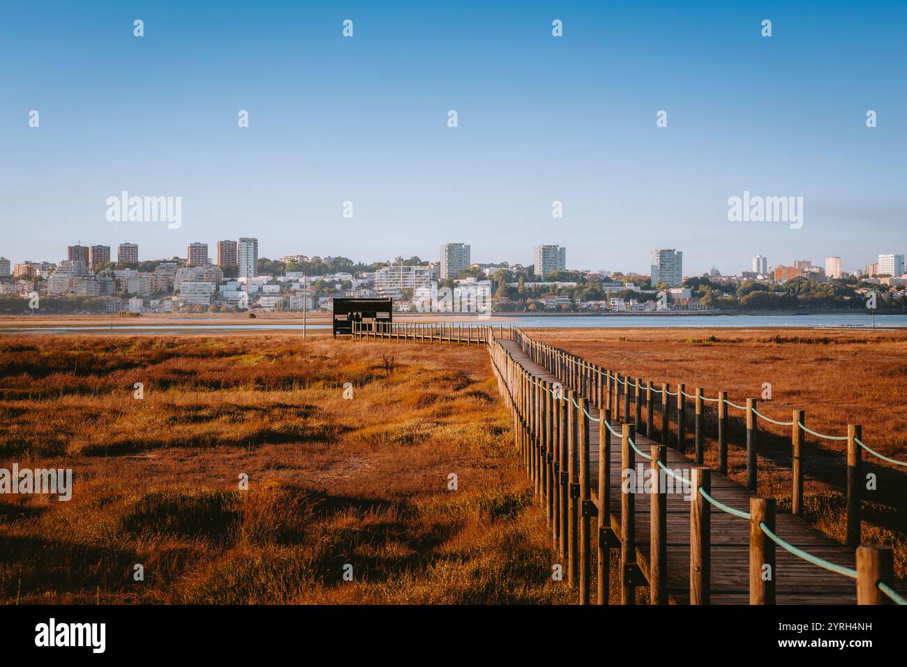 Longue passerelle en bois traversant un marais vers un observatoire d'oiseaux à vila nova de gaia, avec le paysage urbain de porto en arrière-plan sur un ensoleillé Banque D'Images