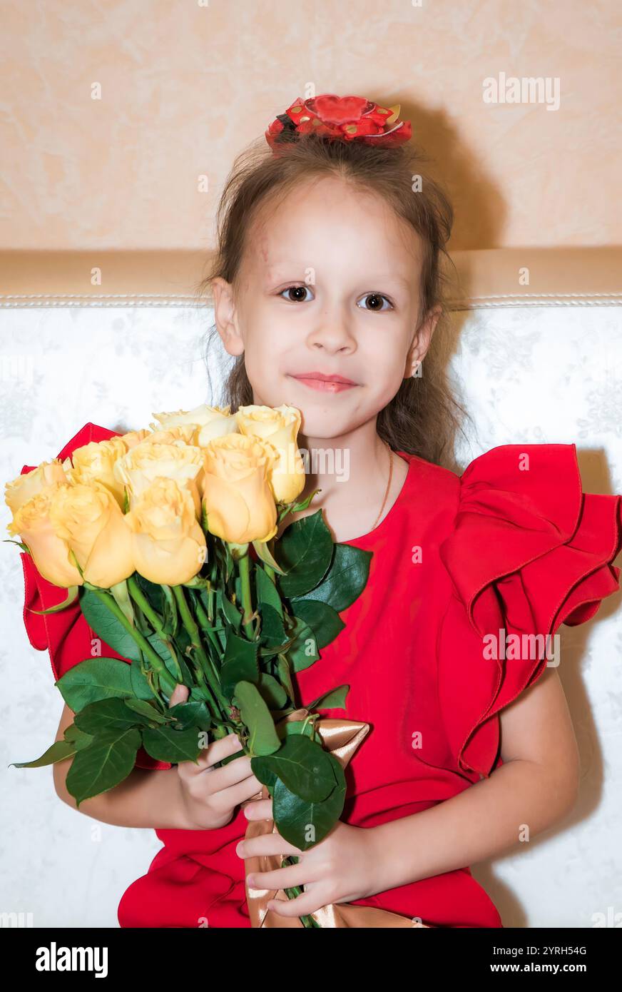 Une jeune fille russe de 8 ans dans une tenue rouge tient un bouquet de roses jaunes, célébrant son anniversaire. Elle regarde la caméra avec une douce expression, Banque D'Images