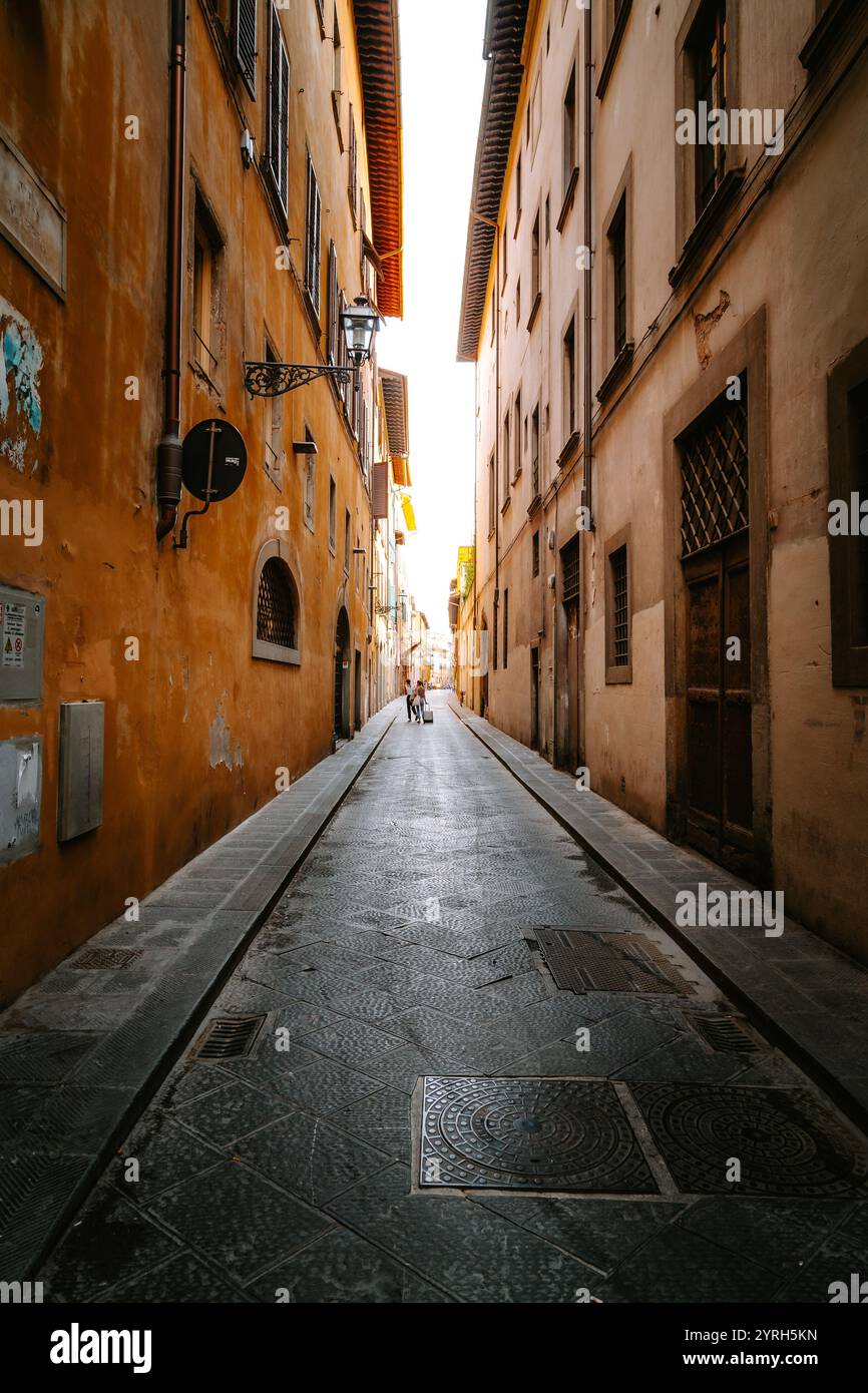 Deux touristes marchant dans une rue pavée étroite à florence, en italie, avec de grands bâtiments de chaque côté, vers la lumière au bout de la rue Banque D'Images