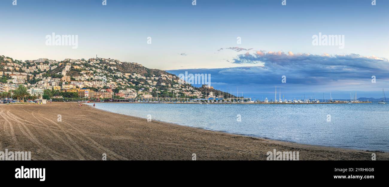 Vue panoramique sur roses, espagne, mettant en valeur la ville nichée sur une colline, une plage tranquille, et des bateaux ancrés dans la baie lors d'un coucher de soleil vibrant Banque D'Images