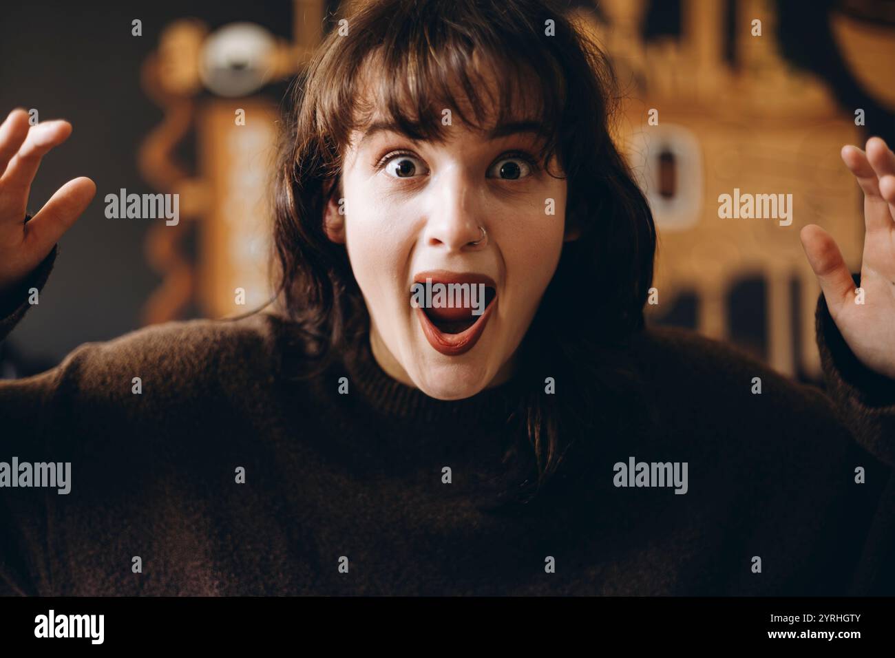 Une jeune femme avec une expression surprise, la bouche ouverte et les yeux larges. Elle se tient sur un fond flou, capturant un moment d'excitation ou Banque D'Images