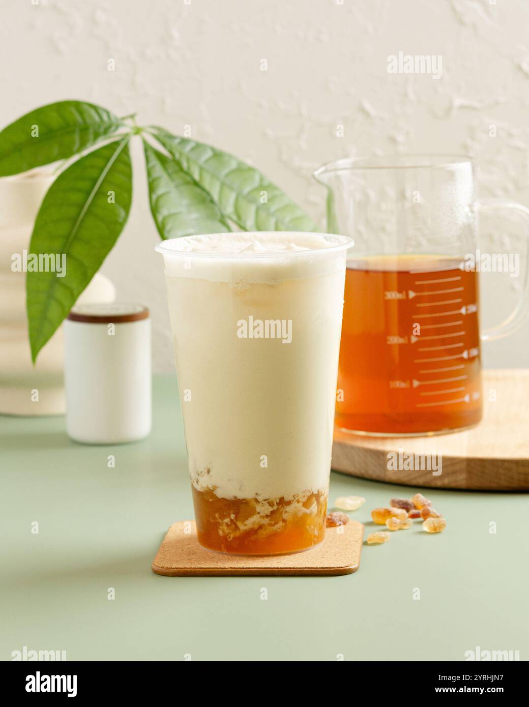 Un thé rafraîchissant au lait glacé garni de crème mousseuse, servi dans une tasse claire gelée ambre repose au fond, accompagné d'un bécher de thé infusé sur un Banque D'Images