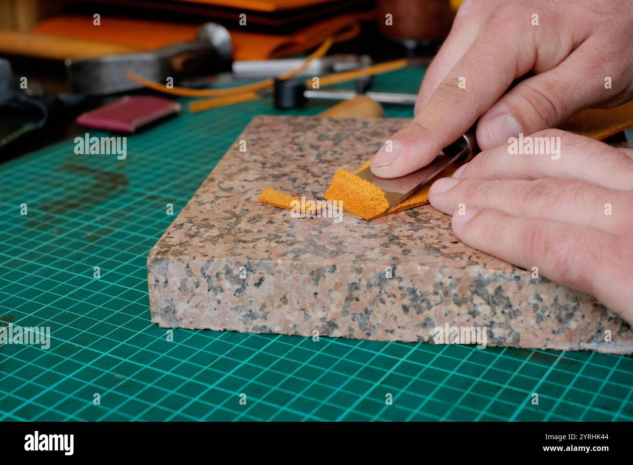 Un artisan habile utilise une lame pour couper un morceau de cuir sur une dalle de granit, mettant en valeur l'artisanat dans la création de maroquinerie outils essentiels sont vis Banque D'Images