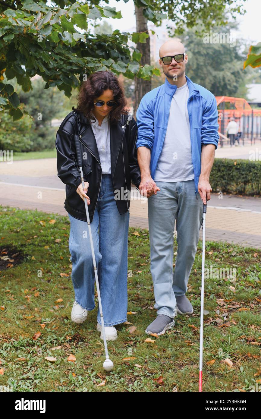 Un couple d'aveugles se promène côte à côte dans un parc, tenant des cannes comme guide. Entourés de verdure, ils font preuve de force, de camaraderie et de RESL Banque D'Images