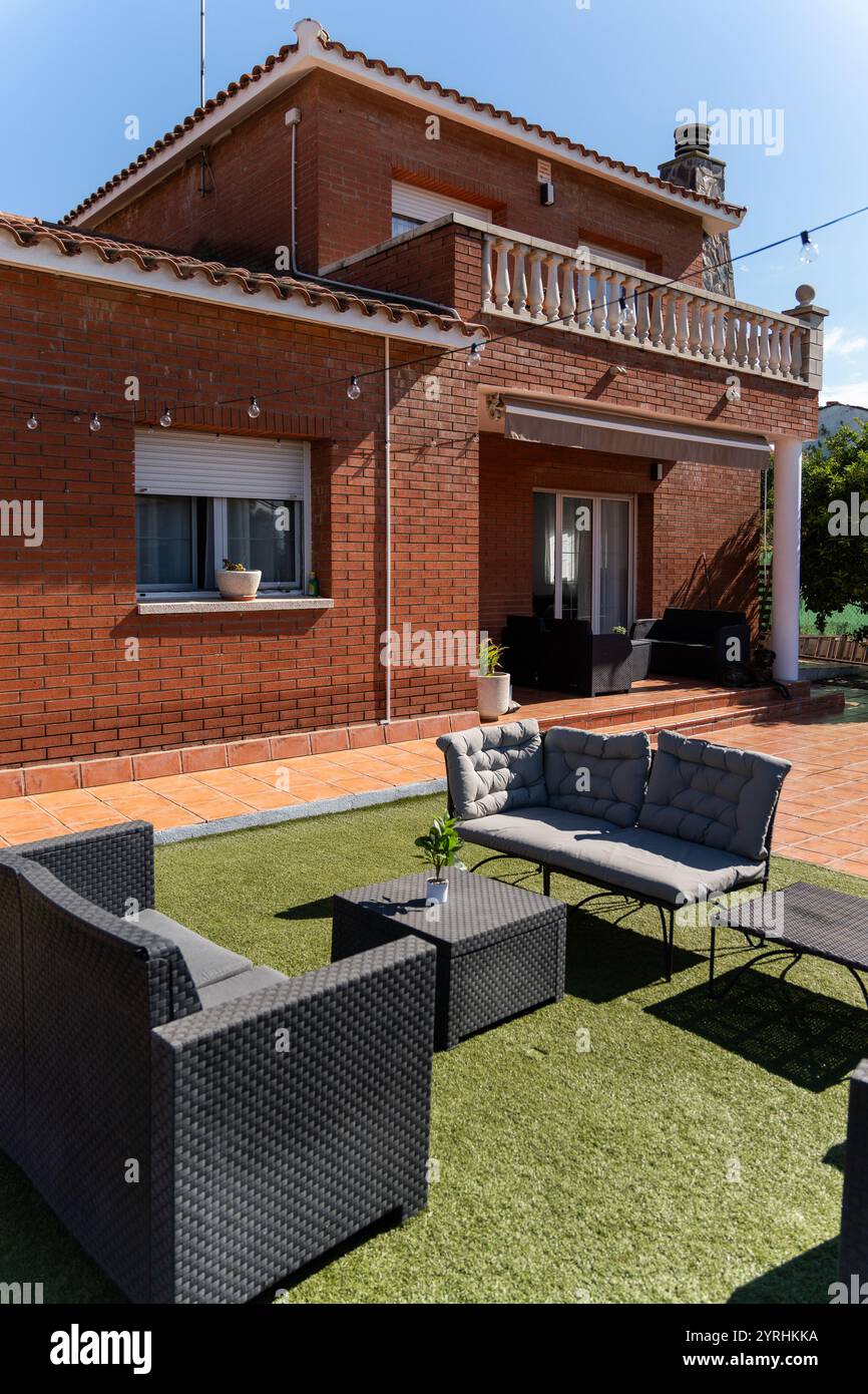 Maison en brique moderne avec un patio confortable avec des sièges extérieurs confortables la scène capture un espace détendu idéal pour les loisirs sous un ciel bleu clair Banque D'Images