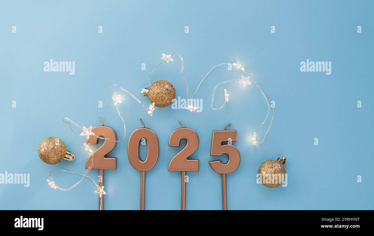 Bougies festives dorées 2025 avec des étoiles lumineuses se trouvent avec des boules dorées sur un fond bleu. Papier peint des fêtes. Nouvel an 2025 et carte de Noël Banque D'Images