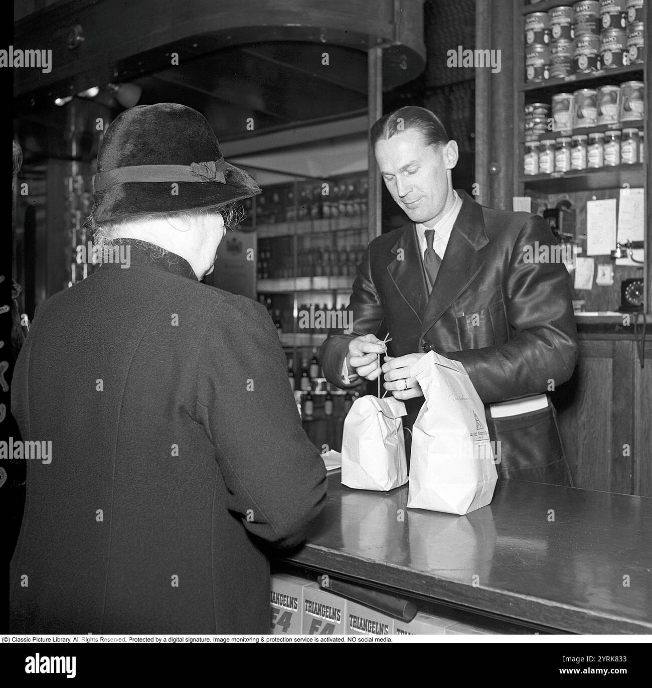 Dans la boutique en 1942. Assistant masculin dans l'épicerie fine d'Arvid Nordquist sur Birgerjarlsgatan à Stockholm. Nous sommes en 1942 et la seconde Guerre mondiale fait rage en Europe. Malgré la guerre, l'entreprise est en mesure de proposer des épiceries et des délices. La boutique n'est pas encore entièrement passée en libre-service et prend la commande au comptoir. On le voit faire des paquets rangés de l'épicerie. 1942. Kristoffersson ref A123-5 Banque D'Images