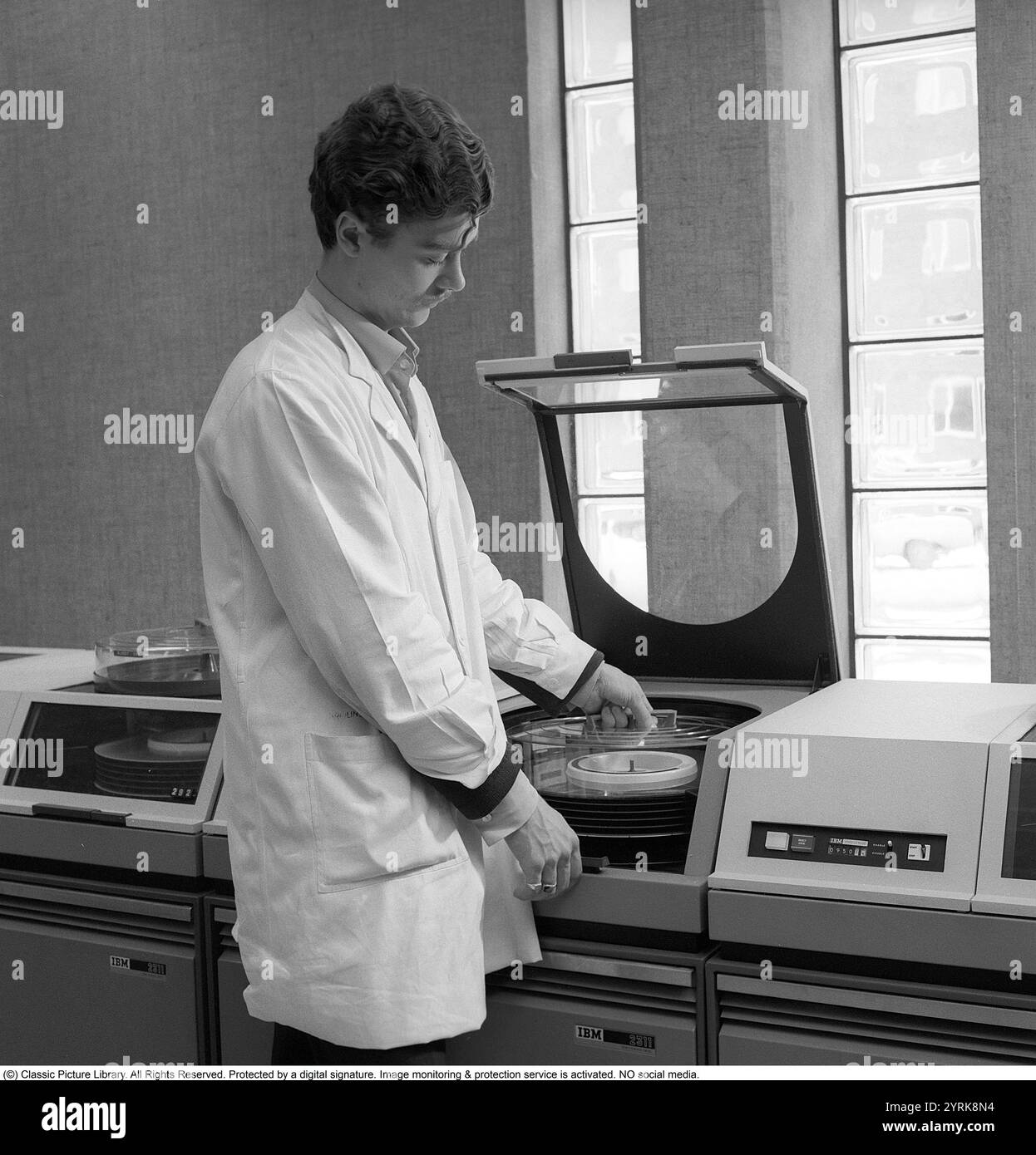 Système mainframe IBM 360. Un homme dans une pièce où une partie du matériel informatique est visible. IBM 2311 Direct Access Storage Facility a été introduit en 1964 pour être utilisé dans toute la famille d'ordinateurs System/360. Il a stocké jusqu'à 7,25 mégaoctets sur un seul pack de disques amovible. Le 2311 est livré avec une interface standard IBM, donnant naissance à toute une industrie de fabricants de lecteurs de disque «plug-compatible» tels que Control Data Corporation et Memorex. Kristoffersson réf. DY127-12 Banque D'Images