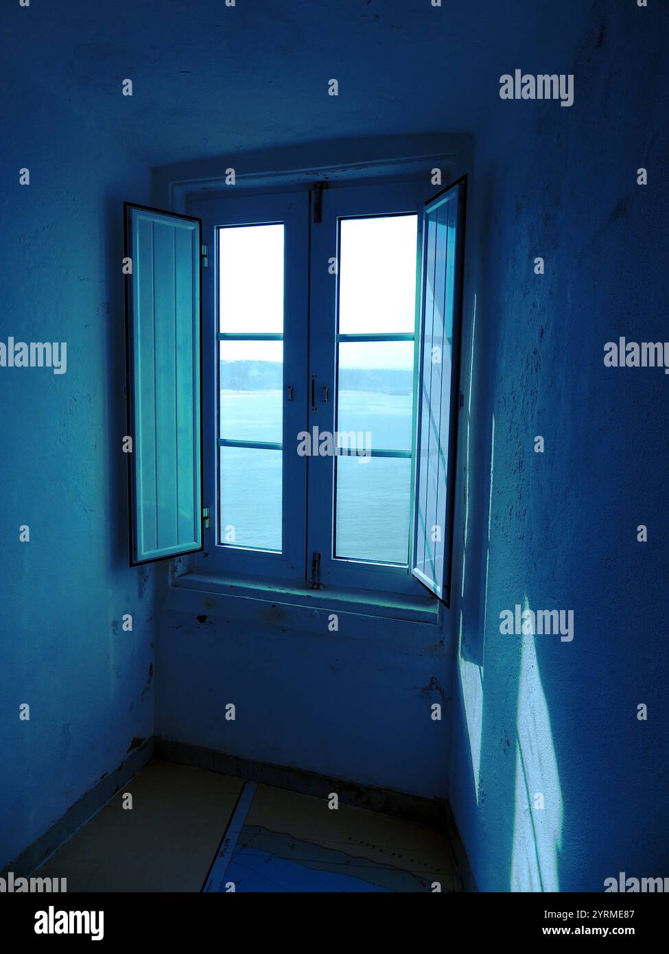 Un intérieur tranquille avec une fenêtre ouverte, une lumière naturelle douce, un design minimaliste, des teintes bleues apaisantes et des murs texturés créant une atmosphère sereine. Banque D'Images