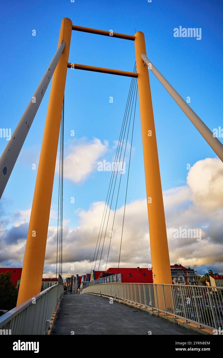 Une vue saisissante d'un pont suspendu moderne avec des piliers orange contre un ciel bleu rempli de nuages à Giżycko, Pologne. Banque D'Images