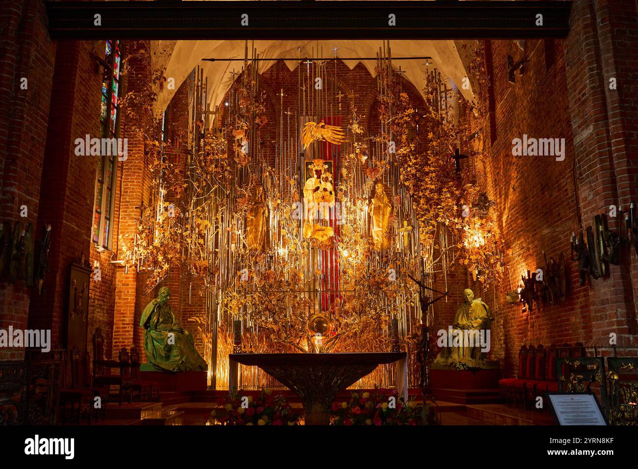 Un intérieur orné d'une église de Gdansk avec un autel magnifique orné de sculptures en ambre doré, de décorations florales et de statues, illuminé par Banque D'Images