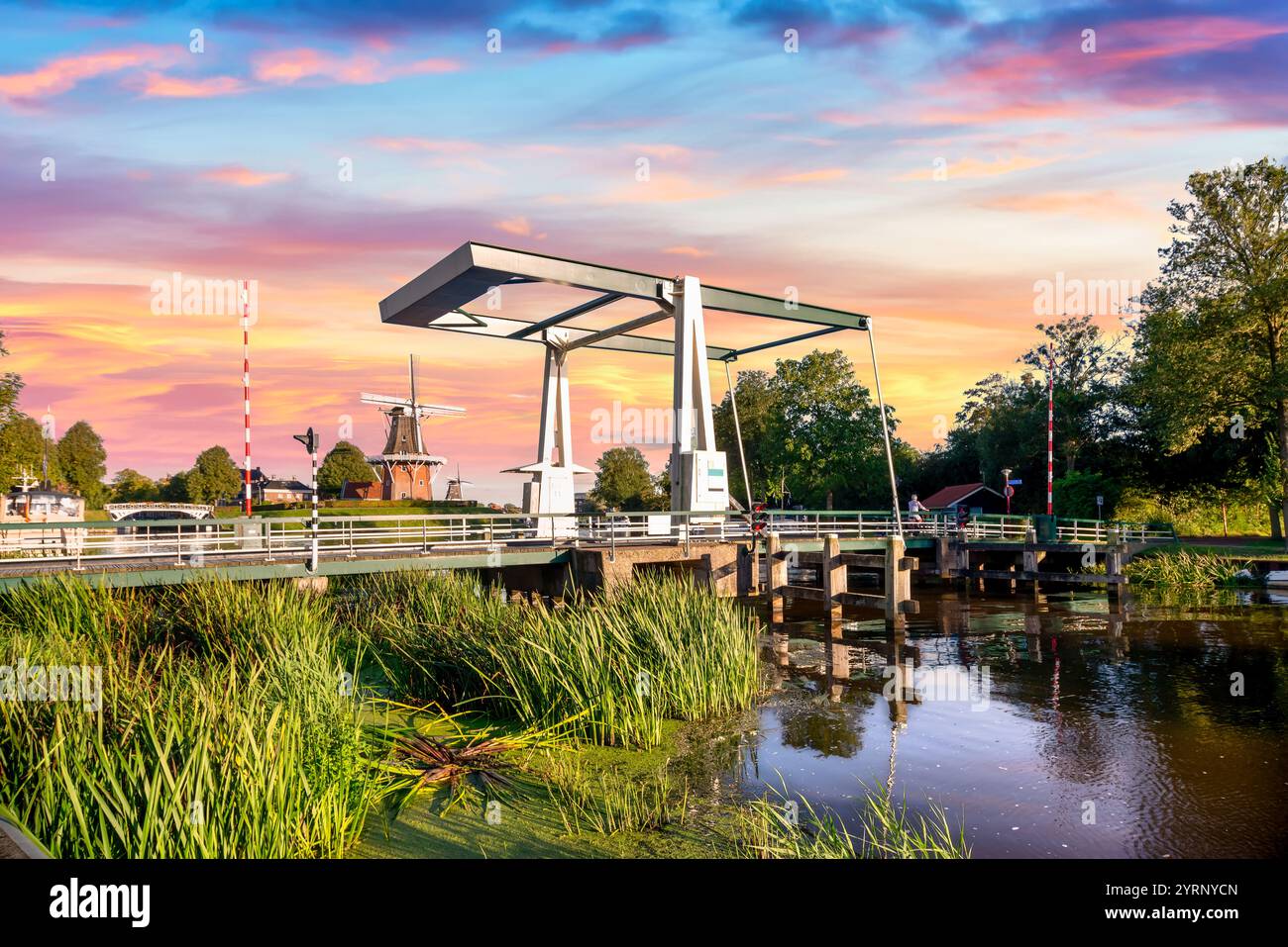 Pittoresque canal hollandais au coucher du soleil avec moulin à vent traditionnel et pont levant Banque D'Images