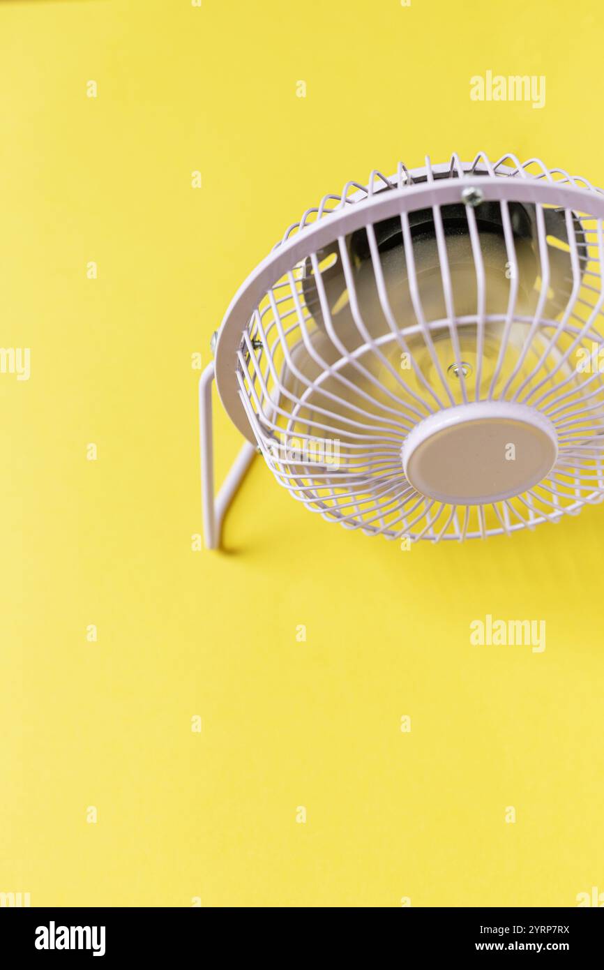 Mini ventilateur créatif se tient et souffle sur un fond jaune. Chauffage et climatisation Banque D'Images