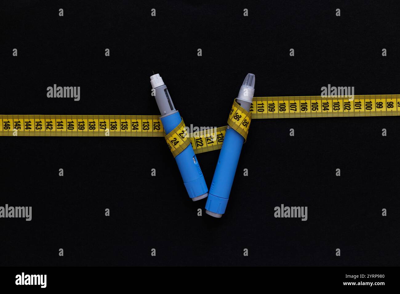 Deux stylos d'injection de drogues ozempic pour la perte de poids avec un ruban à mesurer jaune sur fond noir. Médecine pour diabétiques et perte de poids, vue de dessus. Banque D'Images